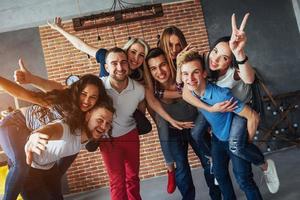 retrato de grupo de meninos e meninas multiétnicas com roupas coloridas da moda segurando amigo posando em uma parede de tijolos, pessoas de estilo urbano se divertindo, conceitos sobre estilo de vida de união juvenil foto