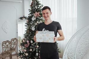 macho segurando uma caixa de presente e sorrindo. conceito de dia de natal. homem bonito na camisa com presente giftbox foto