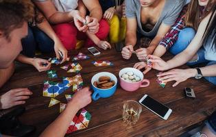 foto criativa de vista superior de amigos sentados à mesa de madeira. se divertindo jogando jogo de tabuleiro