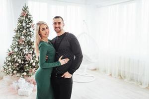 casal jovem feliz no natal, belos presentes e árvore ao fundo foto