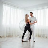 jovem casal dançando música latina bachata, merengue, salsa. duas pose de elegância no quarto branco foto