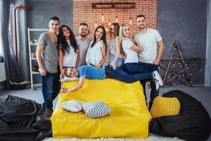 retrato de grupo de meninos e meninas multiétnicas com roupas coloridas da moda segurando amigo posando em uma parede de tijolos, pessoas de estilo urbano se divertindo, conceitos sobre estilo de vida de união juvenil foto