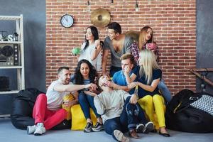 retrato de grupo de meninos e meninas multiétnicas com roupas coloridas da moda segurando amigo posando em uma parede de tijolos, pessoas de estilo urbano se divertindo, conceitos sobre estilo de vida de união juvenil foto