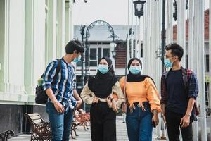 grupo de melhores amigos caminhando juntos e se divertindo usando máscara médica para prevenir o vírus corona. quatro jovens rindo e curtindo seu tempo na cidade. foto