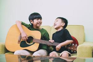 dois irmãos asiáticos se divertindo juntos cantando e tocando violão foto