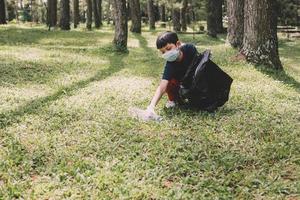 um menino pega lixo de garrafa de plástico e coloca o saco de lixo na floresta, salva o planeta e o conceito do dia da terra foto