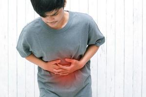 jovem asiático segurando em seu estômago, sofrendo de dor de estômago foto