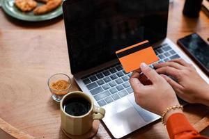 mãos segurando cartão de crédito e usando laptop para pagamento online foto