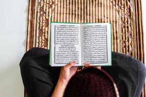 vista superior do homem muçulmano está segurando e lendo o livro sagrado al-quran no tapete de oração foto