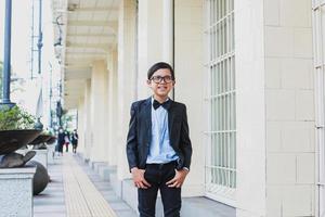 lindo menino asiático vestindo terno preto vintage e óculos posando e sorrindo para a câmera foto