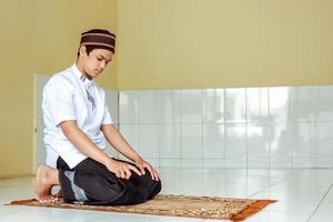 jovem muçulmano asiático fazendo salat no tapete de oração com tahiyat posando cedo foto