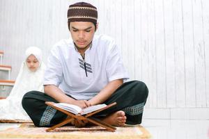 jovem casal asiático muçulmano sentado e lendo o livro sagrado al-quran juntos no tapete de oração em casa. foto