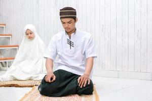 retrato de jovem casal muçulmano fazendo salat juntos no tapete de oração com último tahiyat foto