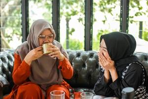 duas mulheres muçulmanas sentadas no sofá, tomando café e brincando