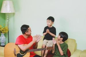 feliz pai asiático cantando e batendo palmas junto com seu filho em casa foto