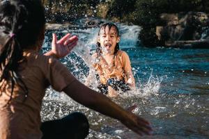 menina asiática brincando no córrego da floresta com a irmã. recreação ativa com crianças no rio no verão. foto