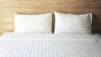 quarto com cama branca, dois travesseiros brancos, edredom branco na cama com cabeceira de madeira e luz solar foto