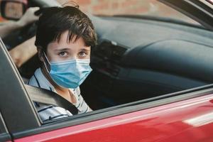 garoto usando máscara médica andando de carro foto