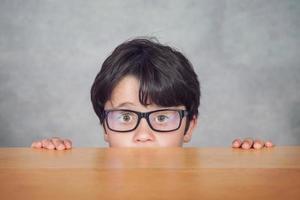 menino com óculos em uma mesa de madeira foto