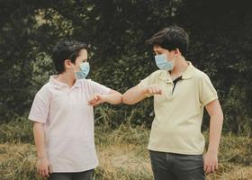 duas crianças com máscara médica batem os cotovelos, conceito de distanciamento social foto