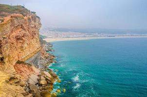 vista aérea de rochas e falésias, água azul-turquesa do oceano atlântico e litoral de praia de areia praia da nazaré foto