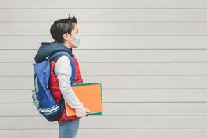 garoto com máscara médica e mochila indo para a escola foto