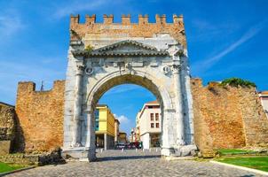 ruínas da antiga parede de tijolos e portão de pedra arco de augustus arco di augusto e estrada de paralelepípedos foto