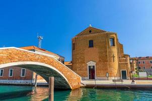 igreja católica de saint domenico e ponte de pedra de tijolo através do canal de água em chioggia foto