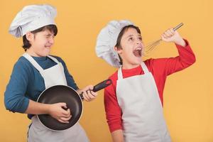 meninos engraçados que cantam com chapéu de cozinheiro segurando o batedor e panela foto