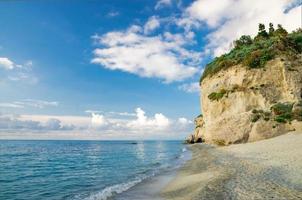 rocha com vegetação perto da praia de areia do mar Tirreno, tropea, itália foto