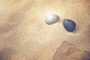 óculos de sol na areia da praia foto