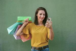 jovem mulher feliz segurando um smartphone e sacolas de compras foto