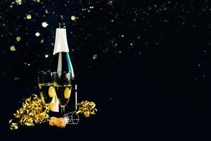 feliz Ano Novo. garrafa de champanhe com duas taças, flâmulas douradas e glitter cintilante com espaço para texto. fundo de conceito de celebração de véspera de ano novo foto