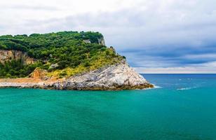 ilha palmaria com árvores verdes, falésias, rochas e água azul turquesa do mar da Ligúria com céu dramático foto