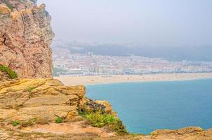 vista aérea de rochas e falésias, água azul-turquesa do oceano atlântico e litoral de praia de areia praia da nazaré foto