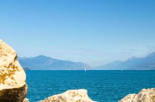 pequeno iate à vela na água azul do lago garda com a cordilheira do monte baldo foto