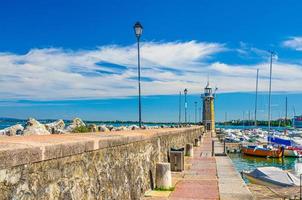 toupeira de cais de pedra com farol, luzes de rua e iates na marina do porto de estacionamento de barcos em desenzano del garda foto