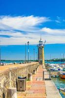 toupeira de cais de pedra com farol, luzes de rua e iates na marina do porto de estacionamento de barcos em desenzano del garda foto