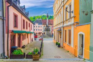 rua estreita da cidade de loket com edifícios típicos tradicionais coloridos, flores de rua e coluna da santíssima trindade foto