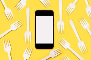 smartphone com tela branca para espaço de cópia com garfos de plástico branco. conceito de entrega de comida foto