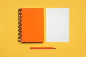 bloco de notas espiral laranja com uma folha de papel branco e lápis laranja foto