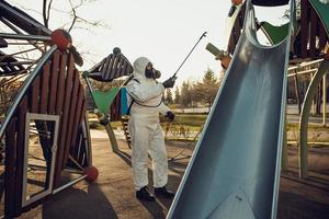 limpeza e desinfecção no playground no complexo da cidade em meio às equipes de epidemia de coronavírus para esforços de desinfecção prevenção de infecções e controle de traje de proteção e máscara epidêmica foto