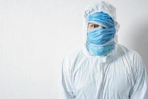 um homem assustado em um traje de proteção pendurado com máscaras médicas retrata o horror contra uma parede branca. os horrores da epidemia, o perigo do coronavírus foto