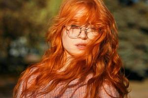 retratos de uma encantadora garota ruiva com óculos e rosto bonito. garota posando no parque outono em um suéter e uma saia cor de coral. a menina tem um humor maravilhoso foto