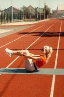 jovem loira agita os músculos abdominais em um tapete esportivo na rua foto
