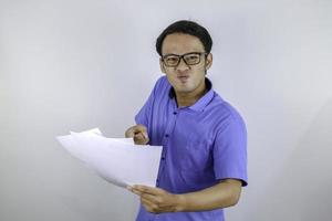 jovem asiático está bravo e com raiva ao olhar no documento em papel. homem indonésio vestindo camisa azul. foto