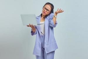 retrato de jovem asiática com raiva falando no celular e segurando o laptop, apontando para copiar o espaço com as palmas das mãos isoladas no fundo branco foto