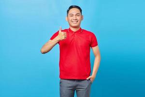 retrato de sorridente jovem asiático mostrando os polegares para cima gesto, aprovando a expressão olhando para a câmera com mostrando sucesso isolado no fundo azul foto