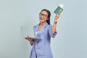 retrato de jovem asiática em pé usando laptop e segurando o livro de passaporte com expressão alegre isolada no fundo branco foto