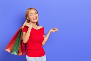 alegre linda mulher asiática de vestido vermelho segurando sacolas de compras isoladas sobre fundo roxo foto